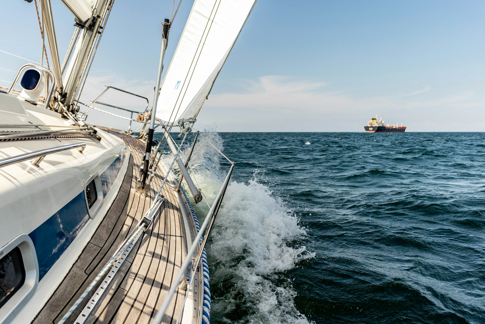Velero a vela navegando en el mar con espuma y un barco al fondo